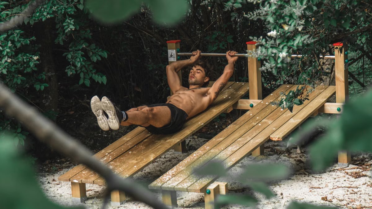 Asian man performing outdoor workout on wooden gym equipment surrounded by nature.
